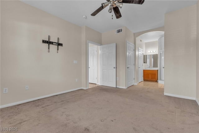 unfurnished bedroom with arched walkways, light carpet, visible vents, baseboards, and ensuite bath