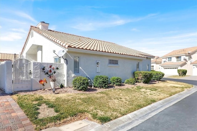 view of side of property with a tile roof, a yard, a gate, stucco siding, and a chimney