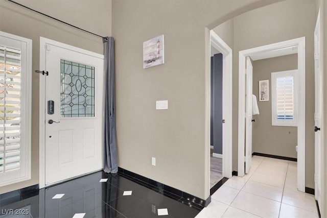 foyer entrance with arched walkways, light tile patterned flooring, and baseboards