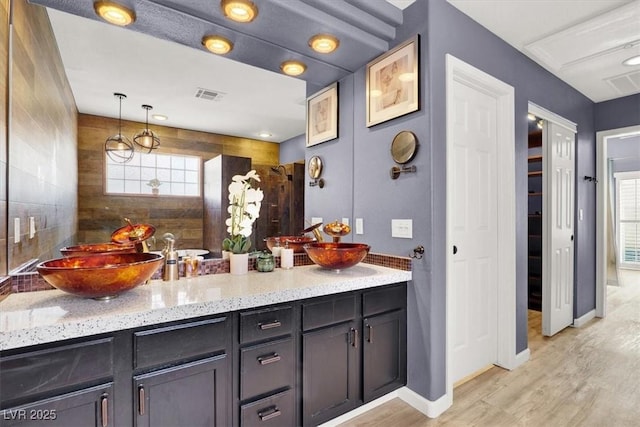 interior space featuring light wood-style flooring, a sink, visible vents, light stone countertops, and pendant lighting