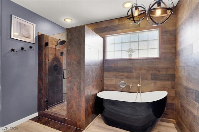 bathroom with baseboards, wood finished floors, an inviting chandelier, a freestanding bath, and a shower stall