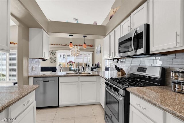 kitchen featuring light stone counters, decorative light fixtures, stainless steel appliances, white cabinets, and a sink