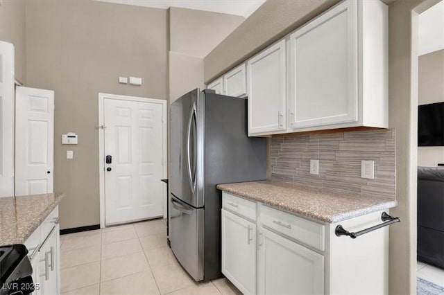 kitchen featuring light tile patterned floors, tasteful backsplash, freestanding refrigerator, light stone countertops, and white cabinetry