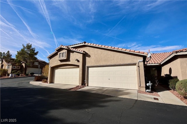 view of front of house featuring a garage, a tiled roof, driveway, and stucco siding