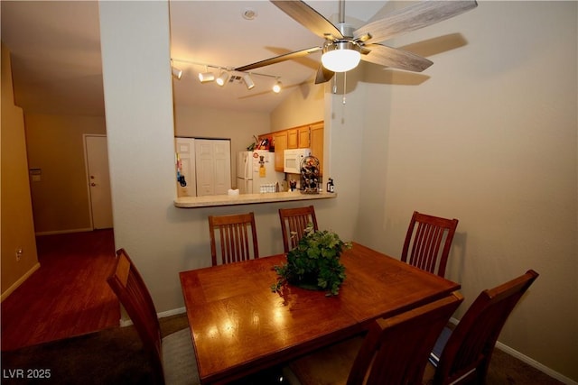 dining room featuring ceiling fan, vaulted ceiling, rail lighting, and baseboards