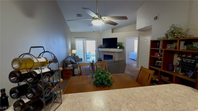 dining room with ceiling fan, vaulted ceiling, a fireplace, and visible vents