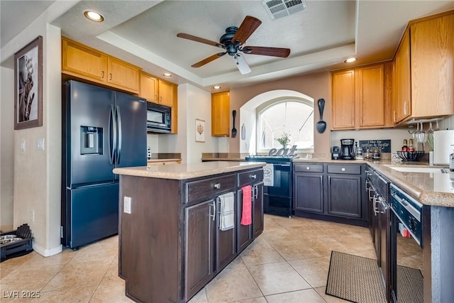 kitchen with black appliances, a tray ceiling, a kitchen island, and visible vents