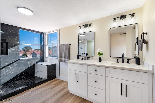 full bathroom with double vanity, a marble finish shower, a sink, and wood finished floors