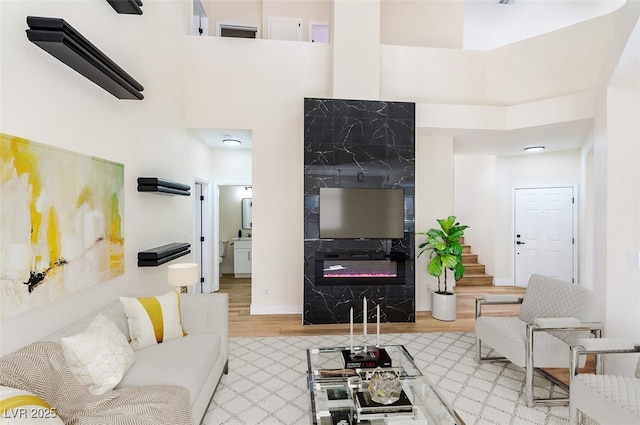 living room with a fireplace, light wood-style flooring, a high ceiling, and stairs