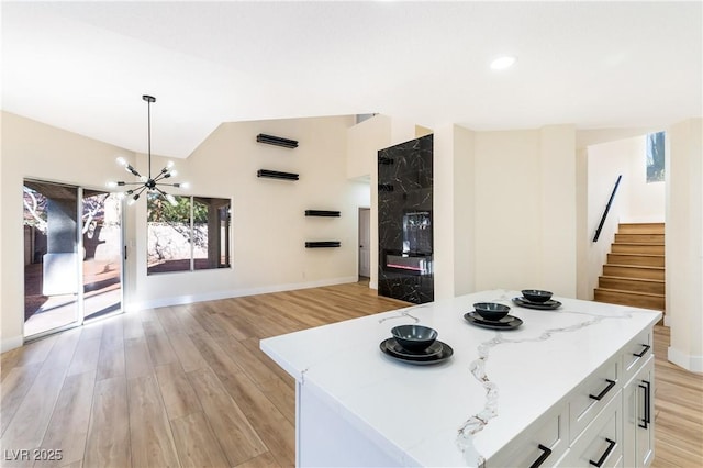 kitchen featuring white cabinets, light wood-style flooring, a kitchen island, light stone countertops, and pendant lighting