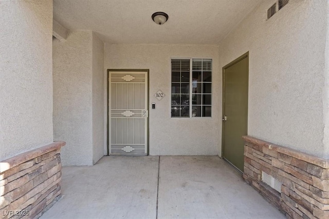 entrance to property with a patio area, visible vents, and stucco siding