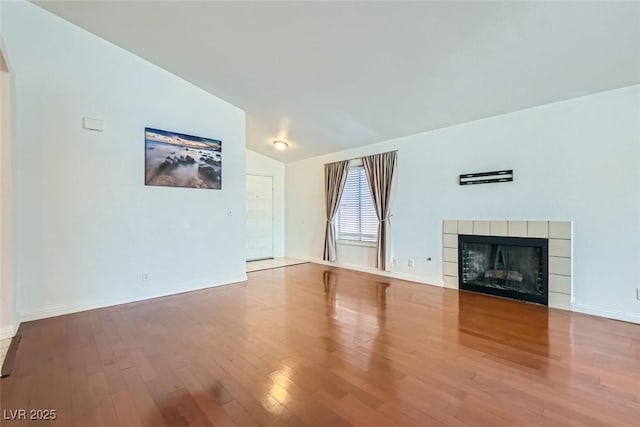 unfurnished living room featuring vaulted ceiling, wood finished floors, a tile fireplace, and baseboards