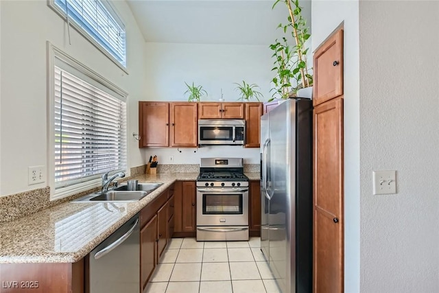 kitchen with light tile patterned floors, light stone counters, appliances with stainless steel finishes, brown cabinets, and a sink