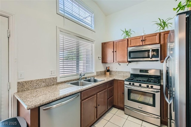 kitchen with light tile patterned floors, stainless steel appliances, a towering ceiling, brown cabinetry, and a sink