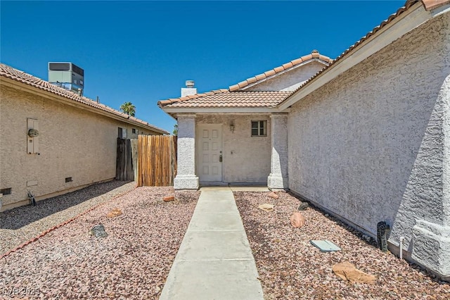 entrance to property featuring a tile roof, fence, central AC unit, and stucco siding