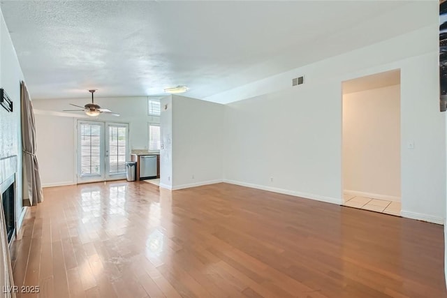 unfurnished living room featuring a fireplace, light wood finished floors, lofted ceiling, visible vents, and ceiling fan