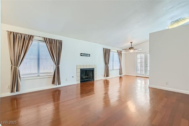 unfurnished living room with a ceiling fan, vaulted ceiling, wood finished floors, a tile fireplace, and baseboards