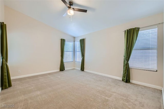 spare room with a ceiling fan, light colored carpet, vaulted ceiling, and baseboards