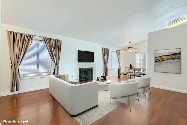 living area with lofted ceiling, a tiled fireplace, wood finished floors, and baseboards