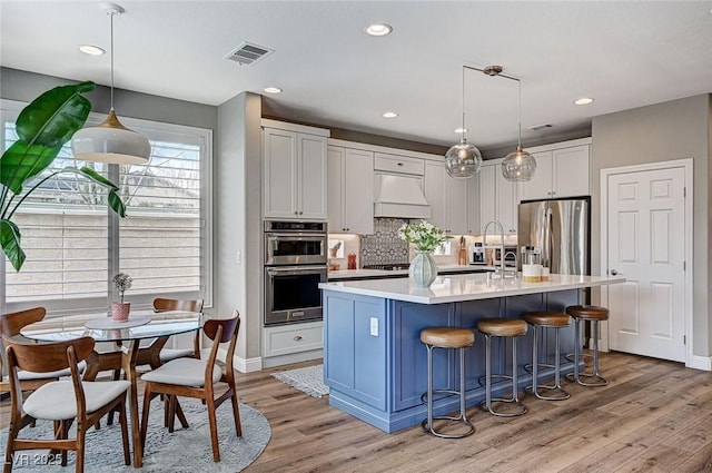 kitchen featuring visible vents, appliances with stainless steel finishes, light countertops, premium range hood, and white cabinetry