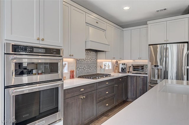 kitchen with stainless steel appliances, white cabinetry, light countertops, custom exhaust hood, and backsplash