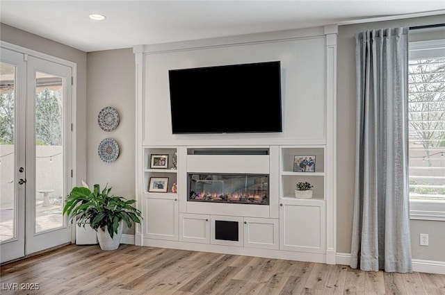 living room featuring a glass covered fireplace, french doors, plenty of natural light, and light wood-style flooring