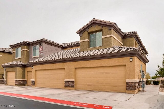 mediterranean / spanish-style home with stone siding, concrete driveway, a tiled roof, and stucco siding