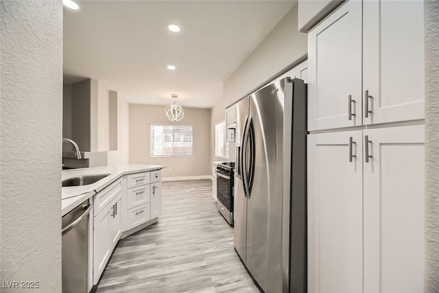 kitchen with light stone counters, a sink, white cabinets, hanging light fixtures, and appliances with stainless steel finishes