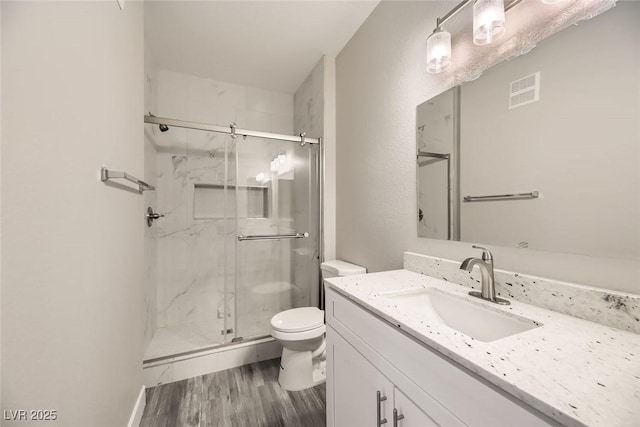 bathroom featuring toilet, a marble finish shower, wood finished floors, and vanity