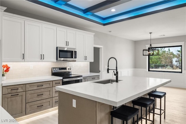 kitchen featuring a center island with sink, a wainscoted wall, a sink, stainless steel appliances, and a kitchen bar