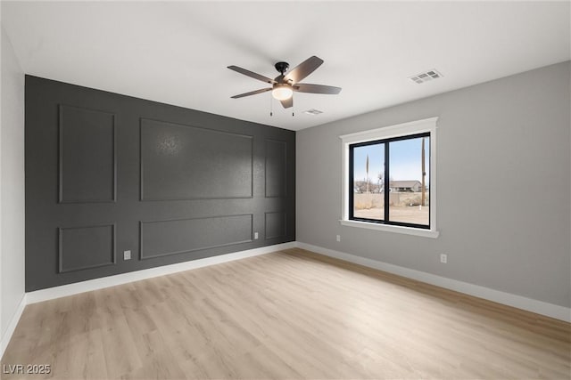 spare room featuring a ceiling fan, baseboards, visible vents, light wood finished floors, and a decorative wall