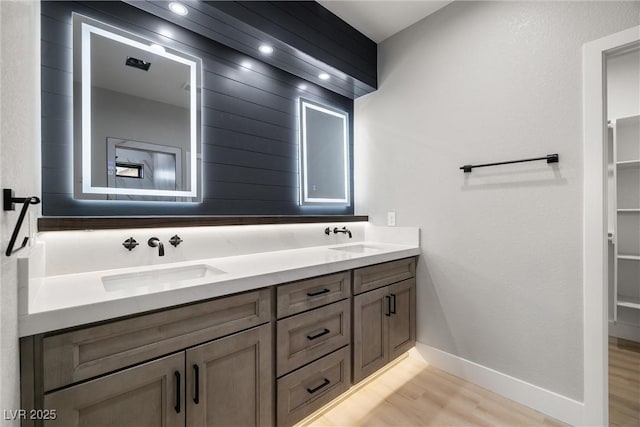 full bathroom featuring double vanity, wood finished floors, baseboards, and a sink