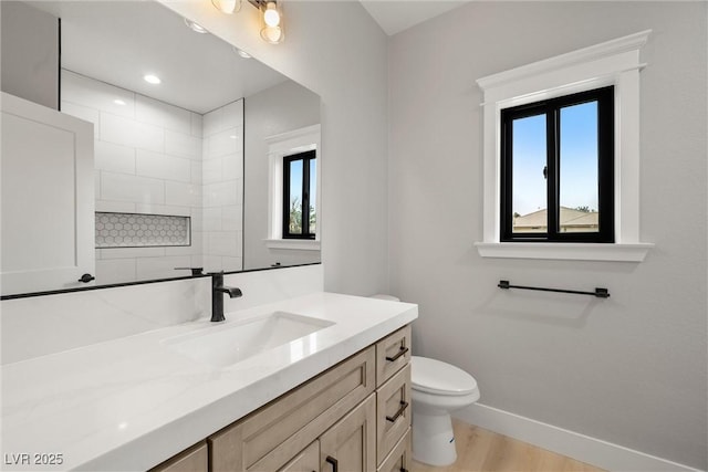 bathroom with toilet, wood finished floors, a tile shower, baseboards, and vanity