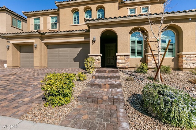 mediterranean / spanish house with an attached garage, stone siding, decorative driveway, and stucco siding