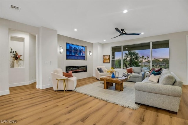 living room with visible vents, baseboards, a glass covered fireplace, light wood-style flooring, and recessed lighting