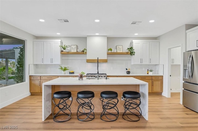 kitchen with open shelves, stainless steel refrigerator with ice dispenser, a kitchen island with sink, and white cabinets