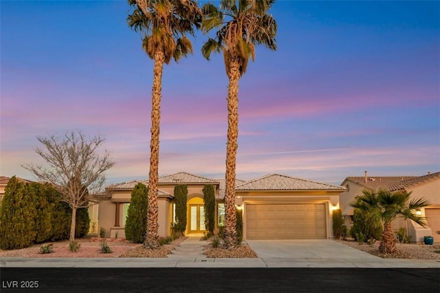 view of front of home featuring a garage, a tile roof, driveway, and stucco siding