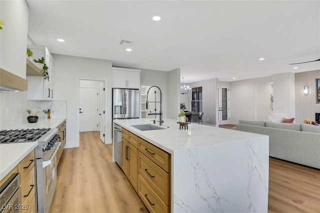 kitchen with stainless steel appliances, a sink, white cabinets, open floor plan, and a center island with sink