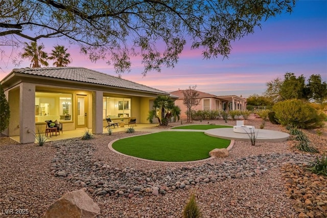 rear view of property featuring stucco siding, a tiled roof, a yard, and a patio