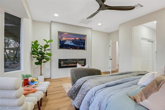 bedroom with recessed lighting, visible vents, wood finished floors, and a glass covered fireplace