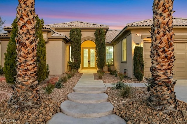 doorway to property featuring french doors, a tile roof, an attached garage, and stucco siding