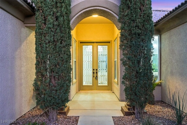 exterior entry at dusk featuring a tiled roof, french doors, and stucco siding