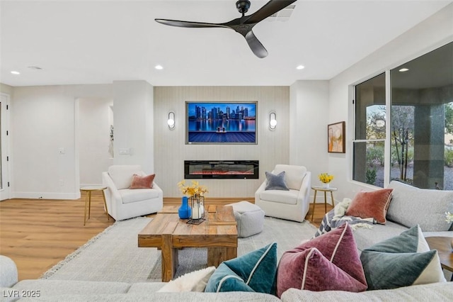 living room with recessed lighting, an accent wall, a glass covered fireplace, light wood-type flooring, and baseboards