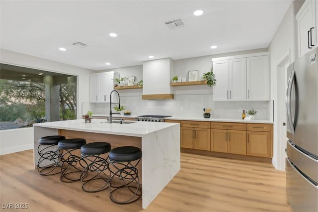 kitchen with freestanding refrigerator, a kitchen island with sink, white cabinetry, open shelves, and a sink