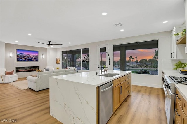 kitchen with a glass covered fireplace, appliances with stainless steel finishes, open floor plan, a kitchen island with sink, and a sink