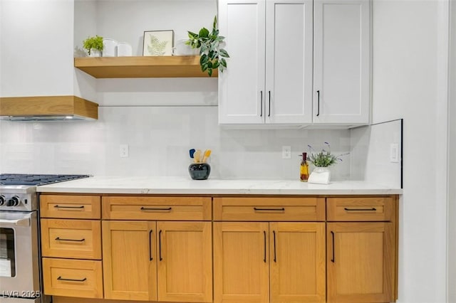 kitchen with light stone counters, open shelves, tasteful backsplash, custom range hood, and stainless steel gas stove