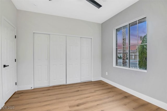 unfurnished bedroom featuring light wood finished floors, a closet, a ceiling fan, and baseboards