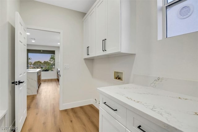 washroom featuring light wood-type flooring, washer hookup, cabinet space, and baseboards