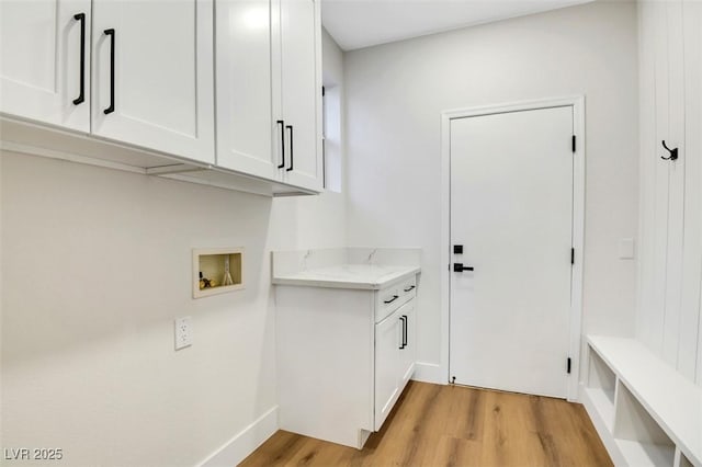 laundry area with baseboards, hookup for a washing machine, cabinet space, and light wood-style floors