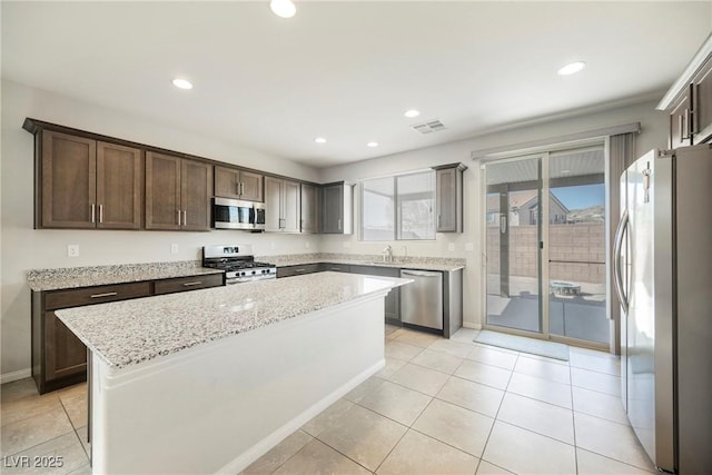 kitchen with visible vents, appliances with stainless steel finishes, light tile patterned flooring, a kitchen island, and light stone countertops